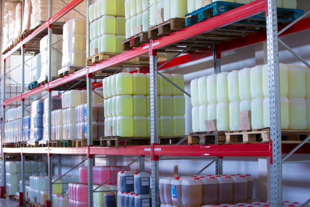 Shelves stocked with large plastic containers of industrial cleaning solutions in a warehouse